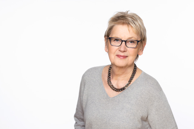 Ein Foto von Ellen Schepp-Winter, die in die Kamera schaut, in Oberkörperansicht mit grauem Pullover und Kette.